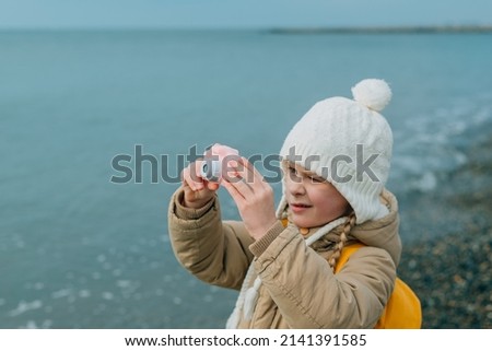 a little girl squinting photographs the autumn seascape on a childrens pink camera. the child is passionately engaged in his hobby: photography. High quality photo