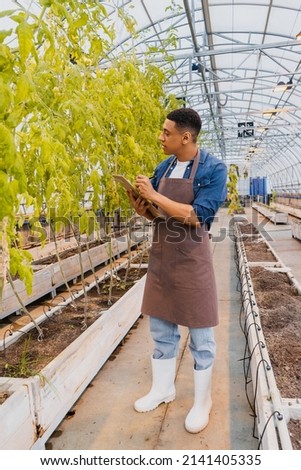 Side view of african american farmer writing on clipboard near plants in greenhouse