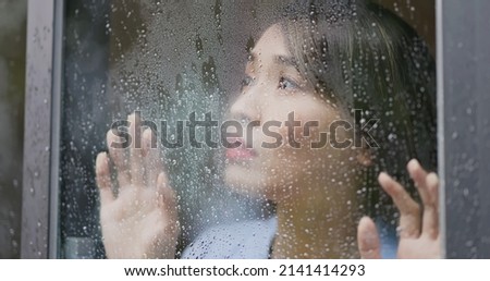 close up view in front of an asian lonely woman looking at the rain falling through a window at home Royalty-Free Stock Photo #2141414293