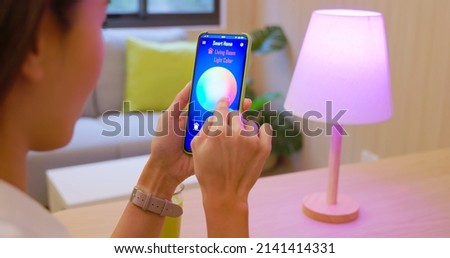 IOT smart home concept - asian woman use app through her smartphone to control the lamp on table