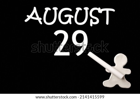 29th day of August. A small white plasticine man writing the date 29 August on a black board. Business concept. Education concept. Summer month, day of the year concept.