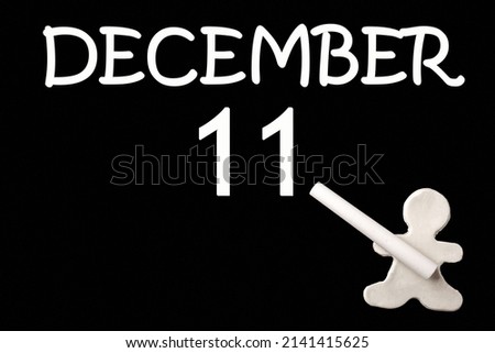 11th day of December. A small white plasticine man writing the date 11 December on a black board. Business concept. Education concept. Winter month, day of the year concept.