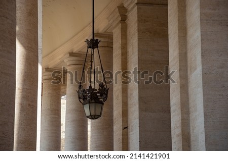 A picture of a chandelier under the Vatican columns.