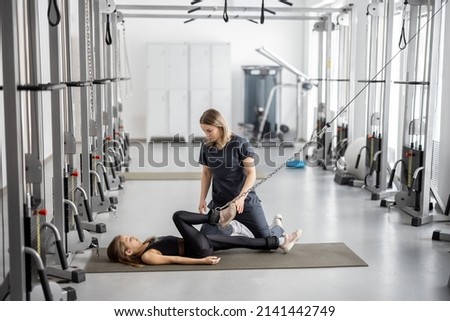 Rehabilitation specialist helping little girl to do exercises on decompression simulators at gym. Concept of physical therapy for back health and posture for kids Royalty-Free Stock Photo #2141442749
