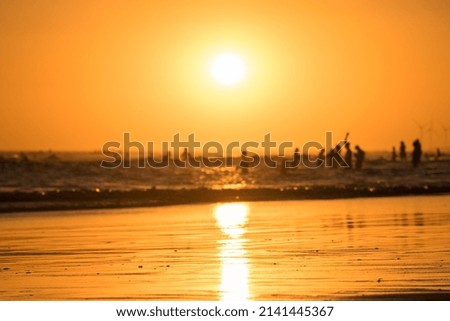 Selective focus on the sand of a sunset on the beach and silhouettes of people in the background in the sea.