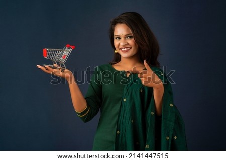 Happy young Smiling girl with a miniature trolley shopping cart on the gray background. Beautiful girl in shopping concept.