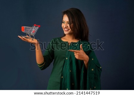 Happy young Smiling girl with a miniature trolley shopping cart on the gray background. Beautiful girl in shopping concept.