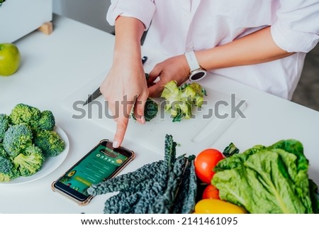 Go vegan. Close up woman cutting broccoli while cooking healthy dish according to the active online mobile application with Vegan diet program on her phone. Healthy lifestyle, weight loss concept Royalty-Free Stock Photo #2141461095