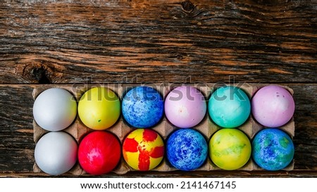 Painted and colored Easter eggs on rustic wooden table inside paper container with copy space above