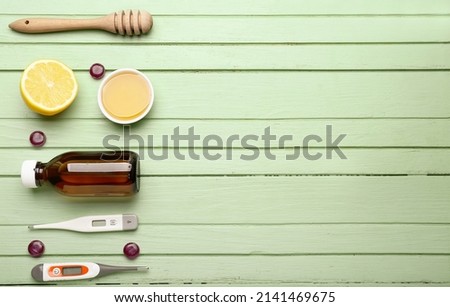 Pills for sore throat, syrup, thermometers and lemons on green wooden background