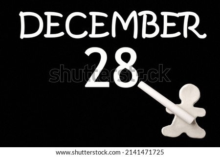 A small white plasticine man writing the date 28 December on a black board. Business concept. Education concept.
