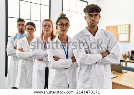 Group of young doctor with serious expression standing with arms crossed gesture at the clinic office.