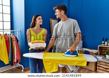 Man and woman couple holding folded clothes ironing at laundry room