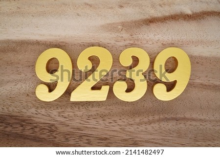Wooden  numerals 9239 painted in gold on a dark brown and white patterned plank background.