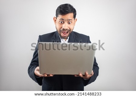 indian man wearing suit looking at laptop screen with surprised expression