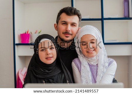 Young father with two child daughter in hijab using a laptop while learning together for school. Happy Muslim family. Smiling dad and kid girl shopping online, have fun at home.