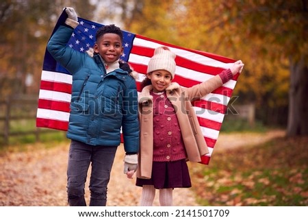 Portrait Of Proud American Boy And Girl Holding Stars And Stripes Flag Outdoors In Autumn