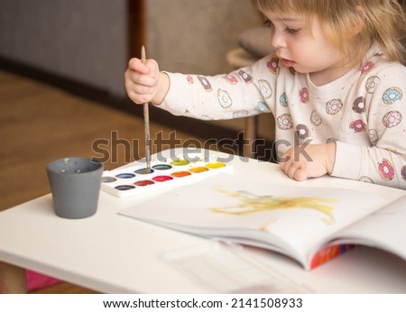 A 2-year-old girl sits at a table and learns to draw with multi-colored watercolors. Children's creativity. Children's hobbies.