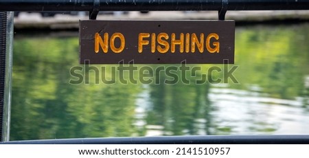 A rectangular wooden sign with orange lettering announces that fishing is not allowed here. Bokeh effect.