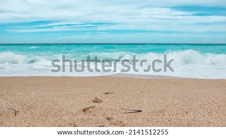 Azure colored waves with blue sky on sunny coast of Greek island. Sandy beach with footprints in Greece. Summer nature vacation travel to Ionian Sea Royalty-Free Stock Photo #2141512255