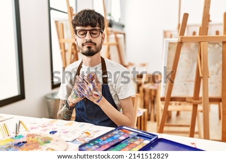 Hispanic man with beard at art studio smiling with hands on chest with closed eyes and grateful gesture on face. health concept. 