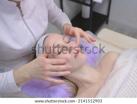 A beautiful girl is lying on the couch close-up, the masseur's hands are doing a modeling lifting. The girl's face is in profile, her eyes are closed, the beautician's palms are near her face. 