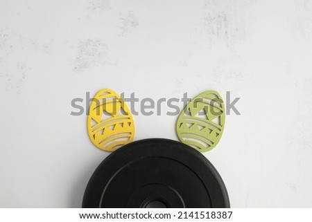 Dumbbells barbell weight plate disc and decorative Easter eggs in shape of bunny ears. Healthy fitness lifestyle rabbit composition, gym workout and training concept. Fit flat lay with copy space. Royalty-Free Stock Photo #2141518387