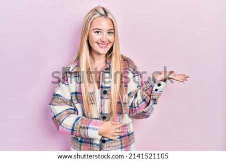 Young blonde girl wearing casual clothes smiling cheerful presenting and pointing with palm of hand looking at the camera. 