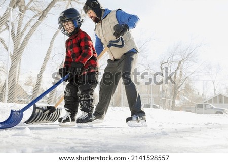 Father and son clearing snow from skating rink with shovels