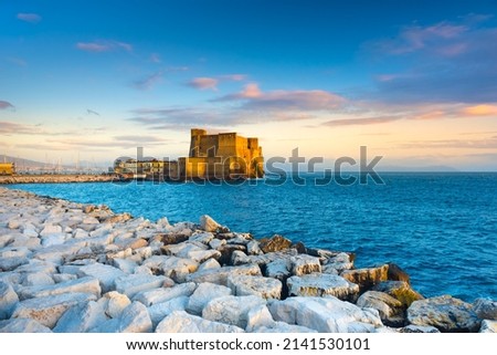 Naples, Italy. Castel dell'Ovo with breakwater rocks in the foreground and with a beautiful sunset sky.  Royalty-Free Stock Photo #2141530101