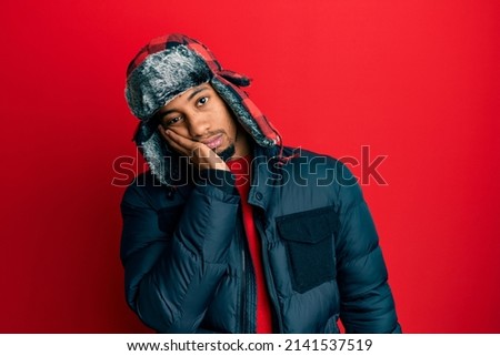 Young african american man with beard wearing winter hat and coat thinking looking tired and bored with depression problems with crossed arms. 