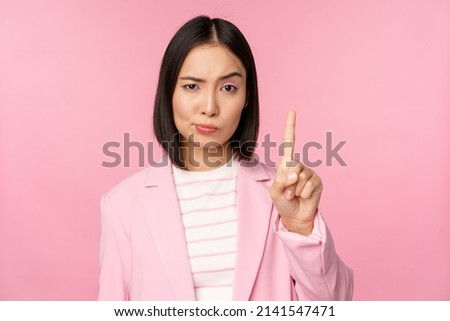 Asian businesswoman with serious, concerned face expression, showing stop motion, taboo, prohibit gesture, disapprove smth bad, standing over pink background
