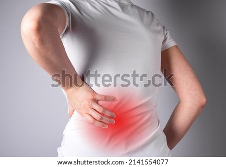 Backache. Woman suffering from lower back pain with red spot closeup. Muscle spasm, sprains, strains, inflammation. Sport, household injury, nervous diseases. Health care and medicine concept. Royalty-Free Stock Photo #2141554077