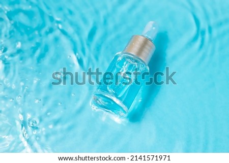 Bottle serum or cosmetic oil in clean transparent water with sunlight on blue background, flat lay, top view, copy space. Cosmetic spa medical skin care concept.