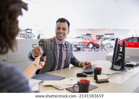 Salesman giving keys to woman in car dealership
