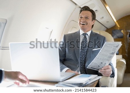 Businessman with newspaper laughing on corporate jet