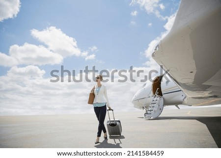 Businesswoman pulling suitcase on tarmac near corporate jet
