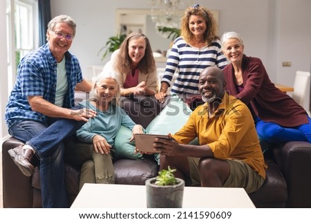 Portrait of smiling multiracial senior male and female friends on sofa at home. unaltered, lifestyle, friendship, leisure, domestic life, social gathering and togetherness. Royalty-Free Stock Photo #2141590609
