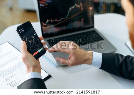 Successful male crypto trader, investor, using a laptop and smartphone, analyzes trading charts in the stock market of a digital cryptocurrency exchange, analyzes, buys and sells cryptocurrencies Royalty-Free Stock Photo #2141591817