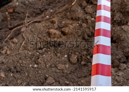 Red and white barrier tape protect a danger place. The warning tape indicates the danger of being on the territory of the construction site. Dug trenches for laying new pipes.