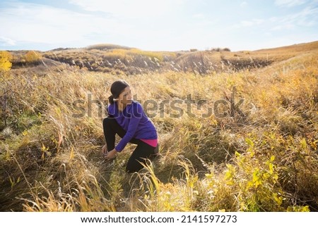 Runner tying shoe in sunny rural field