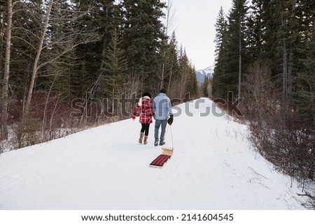 Couple pulling sled down snowy lane in woods