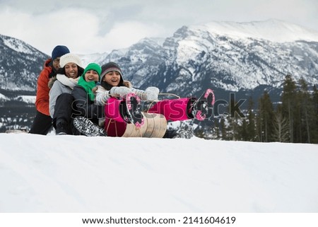 Family sledding down snowy hill below mountains