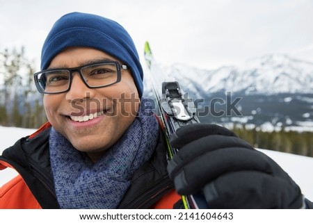 Portrait of smiling man with skis below mountains