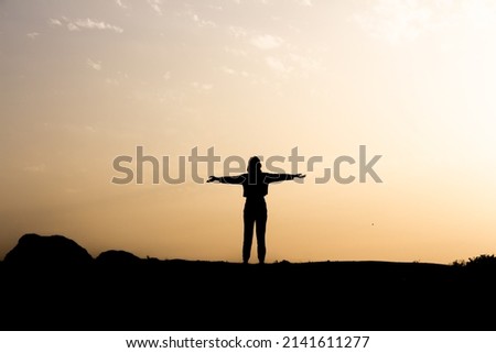 Silhouette of seductive woman on rooftop at urban sunset, Back view silhouette of unrecognizable female in opening hands alone in sunny autumn evening in countryside