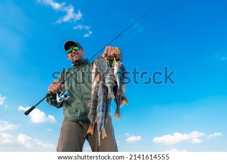 Success perch fishing. Fisherman with many perches and spinning tackle on blue sky background Royalty-Free Stock Photo #2141614555