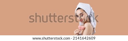 Beautiful girl with thick eyebrows and perfect skin at Calming Coral background, towel on head, beauty photo. Holding a cosmetic pink heart sponge.