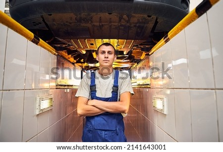 Auto mechanic checking running gear of automobile on service station. Male worker fixing problem with car. Vehicle maintenance concept Royalty-Free Stock Photo #2141643001