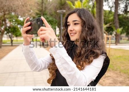 Taking photo with phone, young smiling woman taking photos with her smartphone on city park outdoor.
