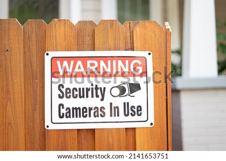 "Warning Security Cameras In Use" Sign on fence outside of house